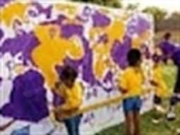 Children in gold shirts painting a large purple and gold mural